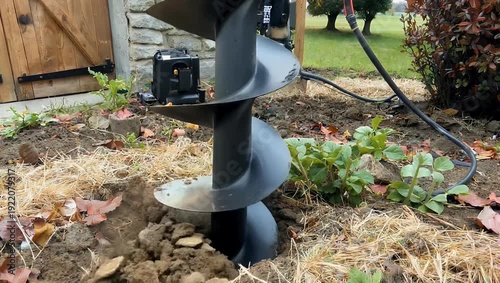 Detailed 4K Ultra HD construction close up view of a large auger drill bit boring deep into the ground showing the process of actively preparing the soil for hedge planting in a private garden area