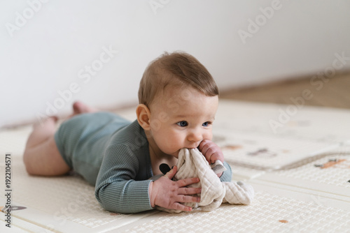 Adorable baby lying on tummy on a soft play mat and playing with a sensory toy. The infant is focused and curious while exploring the toy, supporting early learning and motor skill development.