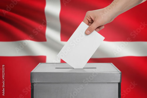 Hand casting vote into ballot box with Denmark flag, democratic process, citizen participation in elections, patriotism