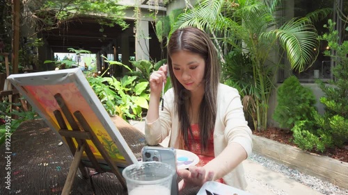Gen Z Influencer content creator woman using smartphone with creativity leisure painting brush on canvas at workshop cafe
