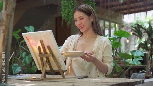 Authentic Gen Z happy young adult asian woman painting brush on canvas at workshop cafe creativity lifestyle therapy