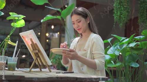 Authentic Gen Z happy young adult asian woman painting brush on canvas at workshop cafe creativity lifestyle therapy