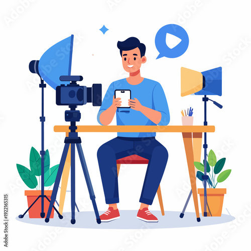 A cartoon man sits at a light brown desk with a camera on a tripod, holding a smartphone, surrounded by reflectors and plants, recording a video in a white studio setting from a side view