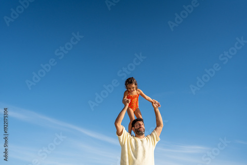 Father and toddler sharing a cute moment under a clear blue sky.