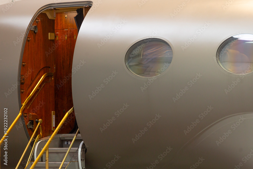 Fototapeta premium Open cabin door gulfstream g boarding stairs extended into hangar, illuminated threshold, polished step rails and warm interior wood contrast with exterior shell