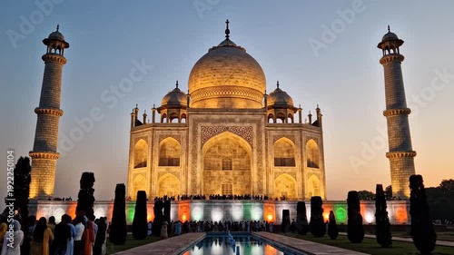 The iconic taj mahal stands majestically illuminated in golden light at twilight, with its reflection in the pool and base subtly lit with patriotic colors in agra, india.