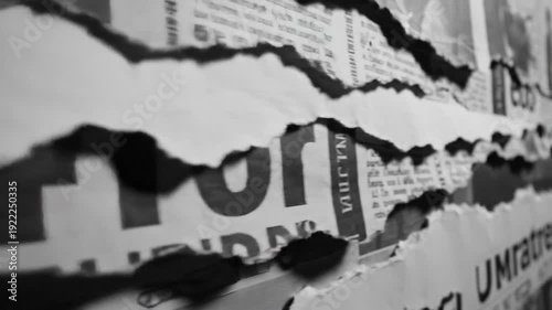 A close-up, monochrome shot highlights the gritty texture of multiple layers of torn paper posters, revealing fragmented text and creating a distressed vintage mood on an urban wall.