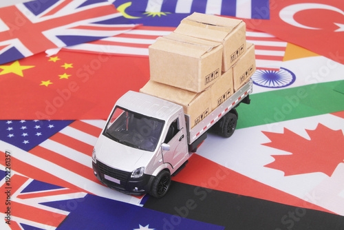 Many cardboard boxes on different national flags and lorry truck. Global trading, shipping and tariffs concept.