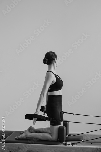 Pilates Reformer machine. Black and white photograph of a slim female executing controlled movements on a specialized Pilates Reformer machine demonstrating strength flexibility and focus