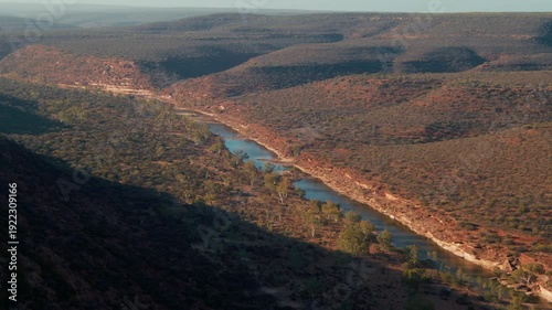 A river flows through hills filled with trees under a clear sky in a remote area during daytime.