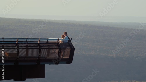 Mother and daughter stands together on a lookout point, taking in the view of the landscape during sunset.