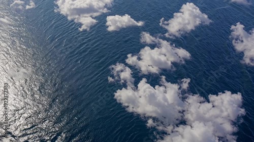 Aerial view of white clouds drifting over a deep blue ocean, showcasing the serene interaction between sky and water in a tranquil coastal environment