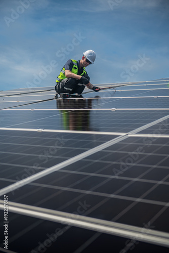 Technician installing solar panels on factory roof for green energy. A skilled technician in safety gear is working on a solar panel installation on rooftop.