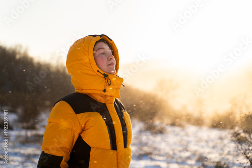 Foto A traveler woman with closed eyes is standing outdoors breathing fresh air during a winter snowfall in the golden sunlight, meditating in the cold weather and feeling gratitude in nature