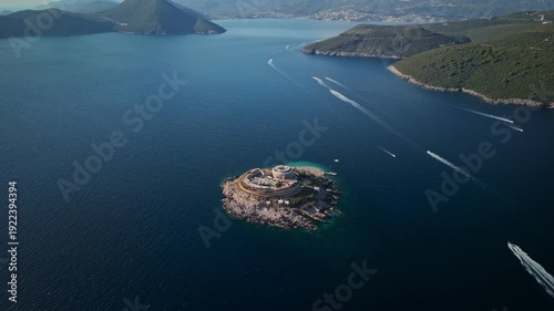 Aerial view of Mamula Fortress on Lastavica near the Bay of Kotor, Montenegro. Speedboats pass, wakes streak the water, wide view shows walls, rim, and coast.