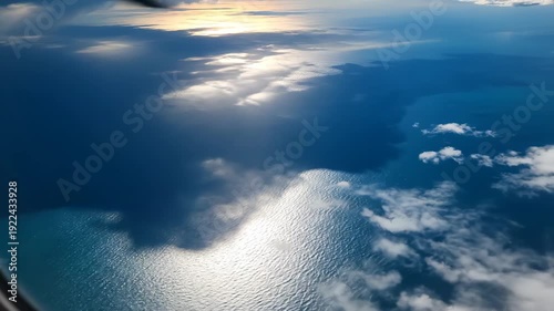 Aerial view of ocean waves reflecting sunlight under a cloudy sky, showcasing the transition of light and shadow across the water surface from above
