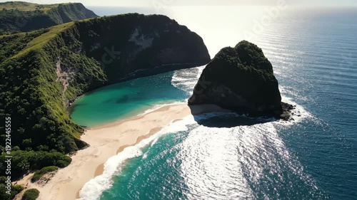Aerial view of a stunning coastal landscape featuring a rocky outcrop, sandy beach, and turquoise waters under bright sunlight, showcasing natural beauty and serenity