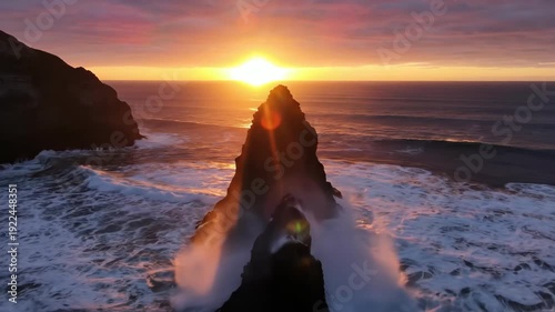 Majestic rock formation rises from ocean waves as sunlight glimmers on water surface during sunrise, creating a breathtaking coastal landscape