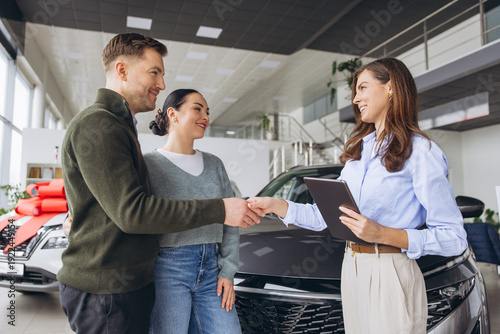 Tableau sur toile Couple celebrating new car purchase in dealership, shaking hands with saleswoman