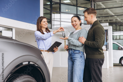 Фотография Saleswoman handing over car keys to happy couple buying new vehicle at modern au