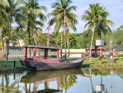 Slika na platnu Traditional Wooden Boat Anchored by a Lake with Coconut Trees  at  Shah Alam Lake Garden, Shah Alam , Selangor