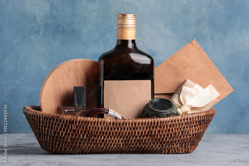 Obraz premium Gift basket with male accessories, bottle of liquor and present on blue table