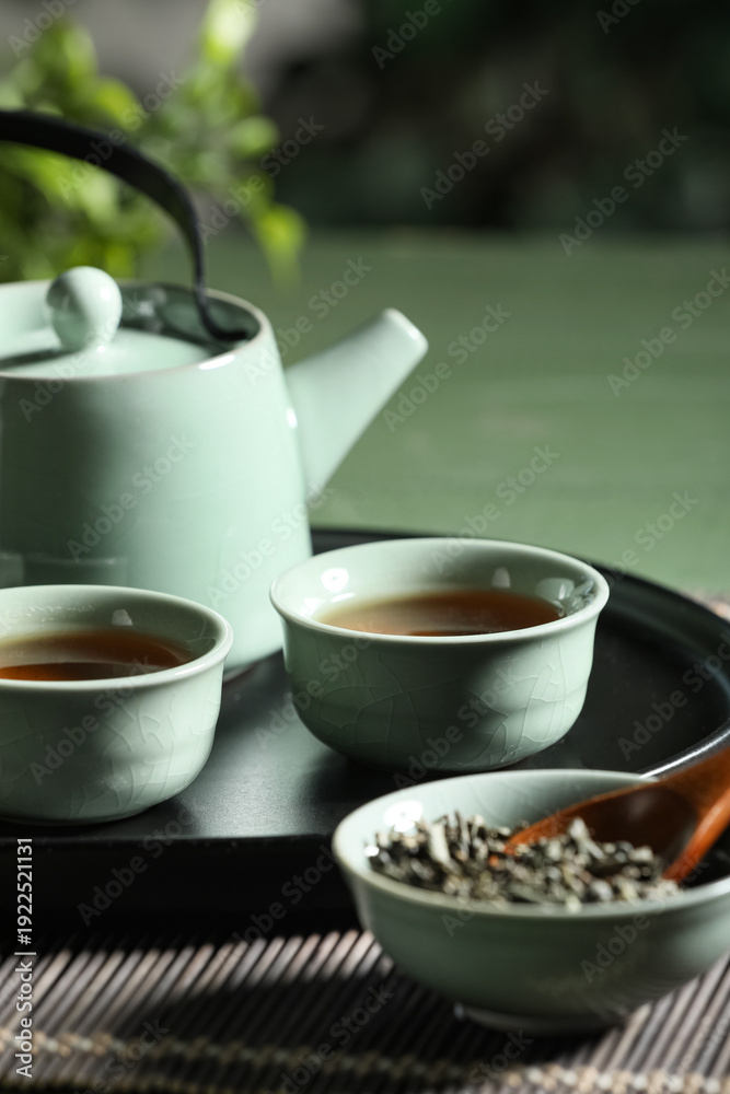 Fototapeta premium Tray with teapot, cups of tea and dry leaves on green table outdoors