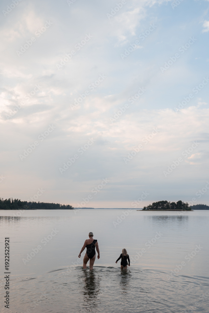 Fototapeta premium Mother and child walking into lake at sunset