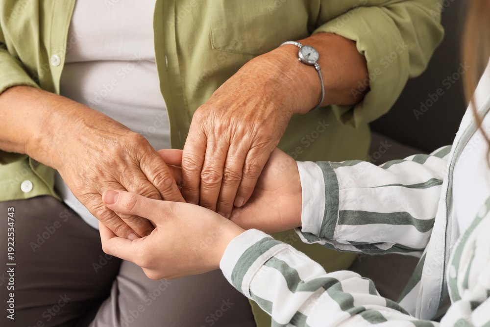 Naklejka premium Young woman with grandmother holding hands at home, closeup. Care concept