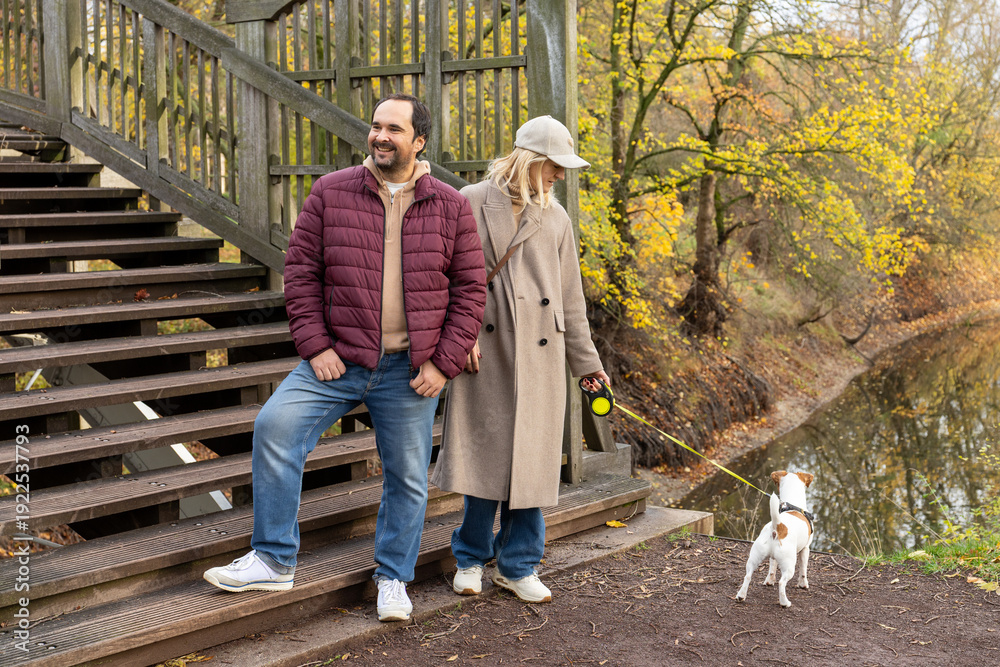 Obraz premium Adult Man And Woman Walking Small Dog Near Wooden Staircase In Autumn Park