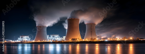 Nuclear power plant cooling towers emitting steam into the night sky, illuminated by artificial lights reflecting on the water