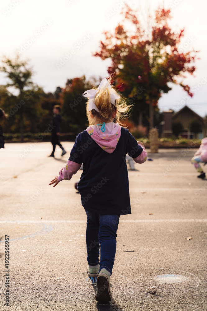 Obraz premium Rear view of young girl running on school playground in autumn