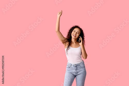 Happy young African-American woman talking by mobile phone on pink background