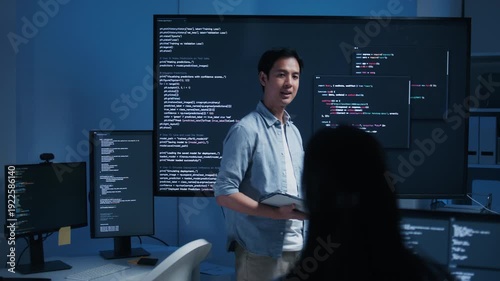 Asian Male Software Engineer presenting code on Screen while Holding Digital tablet and Explaining code, Ai Chatbot Feature, Software Development Task to Colleagues while Collaboration in tech office.