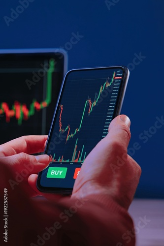 Close up, trader hands holding smartphone with trading application, interacting with a digital stock market charts on a mobile screen. Investing in crypto market, analysis and trading. 