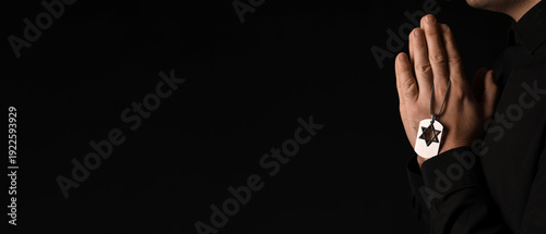 Praying Jewish man with dog tag on dark background, closeup. International Holocaust Remembrance Day