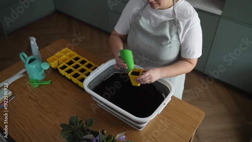 Woman prepares soil for seedlings in the kitchen, home gardening