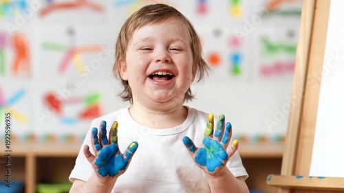 Happy child down syndrome with painted hands laughing joyfully in a creative art class setting.