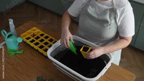 Woman prepares soil for seedlings in the kitchen, home gardening