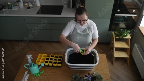 Woman prepares soil for seedlings in the kitchen, home gardening