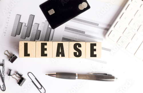 Lease concept written on wooden blocks with office supplies, credit card, charts and calculator