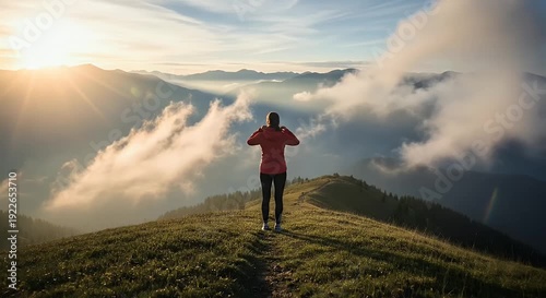 Woman standing on a mountain ridge illuminated by soft golden sunlight over distant mountain range with dreamy clouds offering a sense of peace