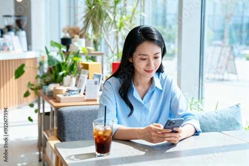 Woman Using Mobile Phone in Café with Iced Drink