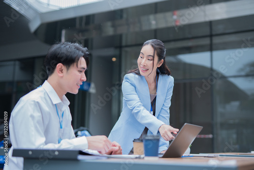  Two business people or a management team are working together using laptops in front of a building.