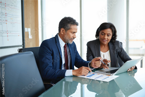 Two busy executive managers working on laptop discussing financial documents at meeting