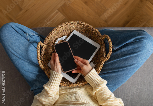 Fotografie Digital detox from gadgets, social media and internet device addiction with woman on sofa at home putting away phone and tablet in basket for healthy lifestyle balance and mental health