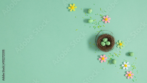 Easter nest with speckled green eggs on mint background with pastel flowers, top view, spring holiday celebration composition Easter with copy space for text, flat lay concept for greeting card design