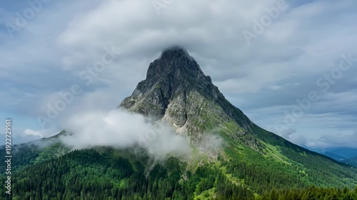 Dramatic mountain peak rising through clouds in green forest landscape - 4k video