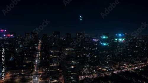 Drones flying over vibrant cityscape at night with illuminated skyscrapers - 4k video