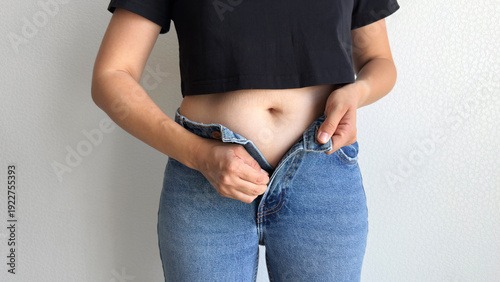 Tableau sur toile Young woman in black crop top trying to button tight blue jeans, close up view o